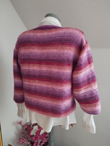 Rückenansicht einer kurz geschnittenen gestrickten Damenjacke mit horizontalen Streifen in Rosa- und Lilatönen auf einer Schneiderpuppe.