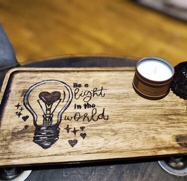 Hell geöltes Holztablett mit graviertem Motiv: Glühbirne mit Herz und dem Schriftzug „Be a light in the world“.