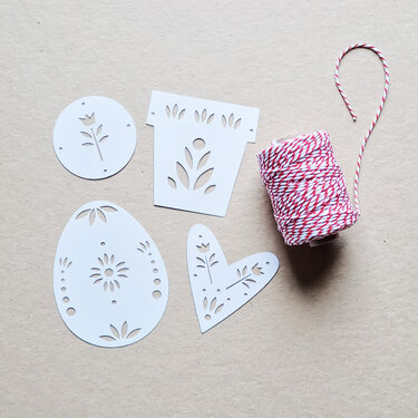 Weiße Plottdateien in Herz-, Ei-, Blumentopf- und Kreisform mit floralen Aussparungen neben rot-weißem Garn