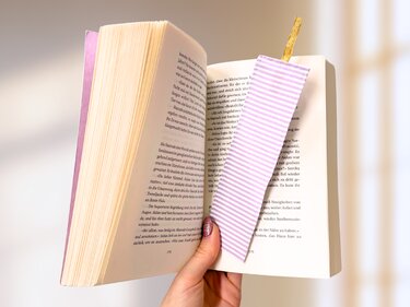 Genähtes Stofflesezeichen gestreift in helllila mit goldfarbener Schlaufe zwischen den Seiten eines Buchs