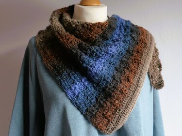 Gehäkeltes Dreieckstuch mit Farbverlauf in Blau, Braun und Grau auf einer Schaufensterpuppe.