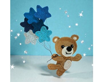 Whimsical crocheted bear holding several blue, dark blue, and light grey star-shaped crochet motifs on strings