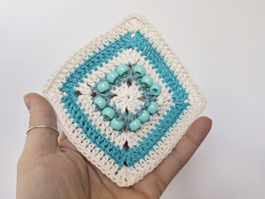 Hand holding a beaded crochet granny square in cream and teal with aqua beads.