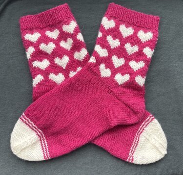 Handgestrickte pinke Socken mit weißen Herzen, gekreuzt auf dunklem Stoff