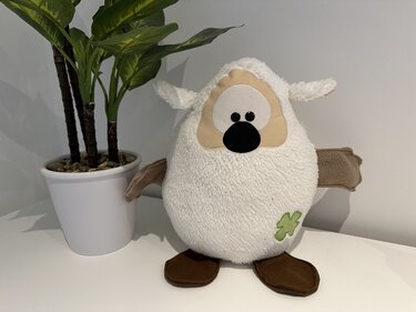Rundes cremefarbenes Kuscheltier mit appliziertem grünen Kleeblatt und braunen Füßen