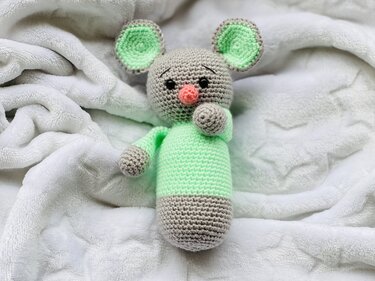 Gehäkeltes Amigurumi-Mäuschen in Grau und Mintgrün auf weißer Kuscheldecke