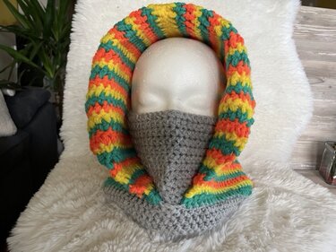 Häkelmuster: Kapuzen‑Sturmhaube mit gestreifter Kapuze (Gelb, Orange, Türkis) und grauem Halswärmer auf Schaufensterpuppe