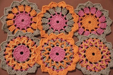 Sechs runde gehäkelte Untersetzer in Pastellfarben (rosa, orange, hellgrün) arrangiert