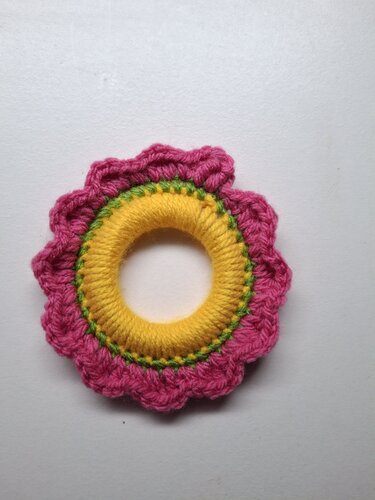 Crocheted baby handring in pink, yellow, and green on a light neutral background.