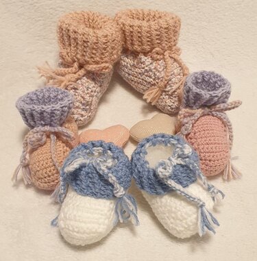 Drei Paare gehäkelter Babyschuhe in Pastellfarben auf hellem Stoff