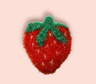 Gehäkelte rote Erdbeere mit grünen Blättern aus flauschigem Garn vor hellem Hintergrund