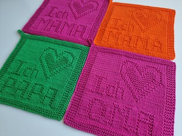 Vier gestrickte quadratische Untersetzer in Pink, Grün und Orange mit Herz-Relief sowie den Schriftzügen MAMA und PAPA