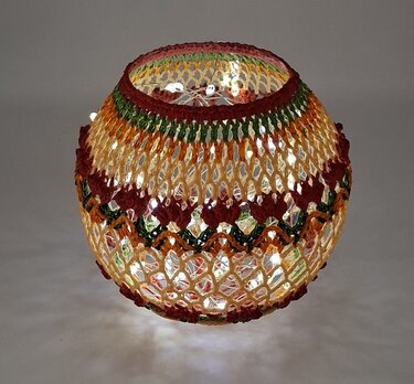 Gehäkelte Dekokugel mit Lichterkette in Herbstfarben, warmes Licht vor neutralem Hintergrund