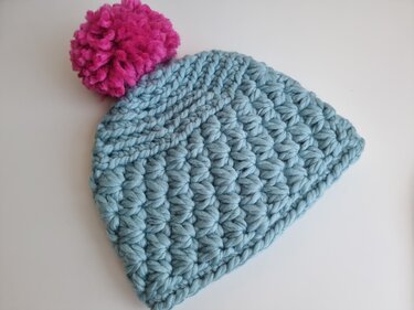 Gehäkelte Beanie in Hellblau mit strukturierten Maschen und pinkem Bommel