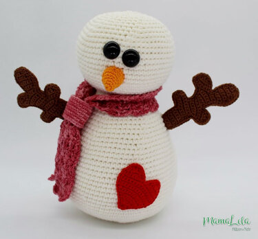 Nahaufnahme eines gehäkelten Amigurumi-Schneemanns mit Herz, rosa Schal und braunen Armen