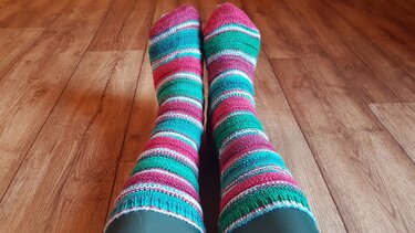 Bunte gestrickte Ringelsocken in Türkis, Grün und Rosa auf Holzfußboden