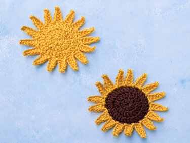 Zwei runde, gehäkelte Applikationen auf blauem Hintergrund: Eine gelbe Sonne und eine gelb-braune Sonnenblume.