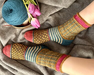 Gestrickte mehrfarbige Damensocken mit Streifen, kontrastfarbener Spitze und Garnknäuel auf grauem Stoff