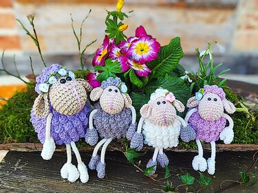 Osterdekoration mit vier gehäkelten Schaf-Amigurumis in Pastellfarben auf Moos vor Frühlingsblumen
