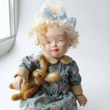 Handmade clay doll with blonde curly hair, blue floral dress, holding a small brown felted rabbit.