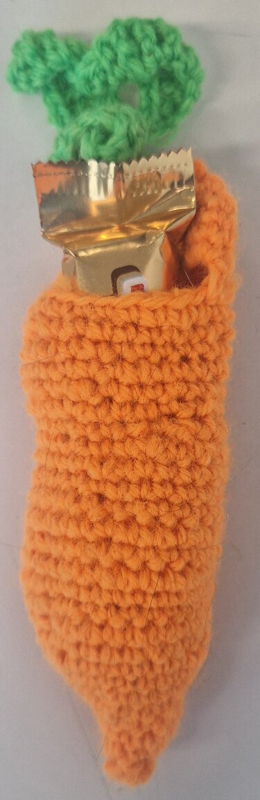 Gehäkelte orange Karotte mit grünen Blättern und goldener Süßigkeitenverpackung