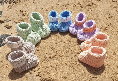 Mehrere Paare gehäkelter Babyschuhe in Pastellfarben auf Sand