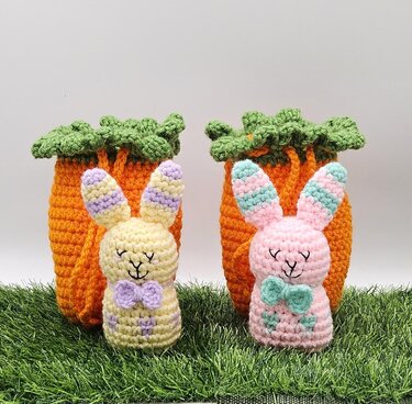 Two pastel crocheted amigurumi bunnies with orange carrot-shaped holders on grass