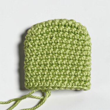 Nahaufnahme eines hellgrünen gehäkelten Stücks mit abgerundeter Oberkante und losen Fäden