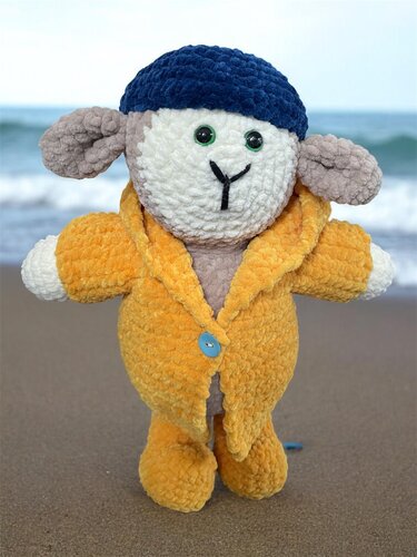 Gehäkeltes Amigurumi-Schaf aus Chenillegarn mit gelbem Mantel, hellblauem Knopf und dunkelblauer Mütze
