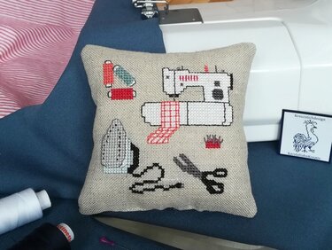 Kreuzstich-Vorlage auf Kissen mit Nähmaschine, Schere, Bügeleisen und Garn