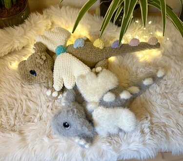 Zwei fantasievolle gehäkelte Drachen auf einer flauschigen Decke, umgeben von warmen Lichtern