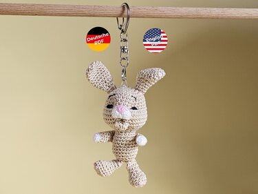 Beiger gehäkelter Hasen-Anhänger mit Metallring, gut sichtbare Maschen; Icons für deutsche und englische PDF-Anleitungen
