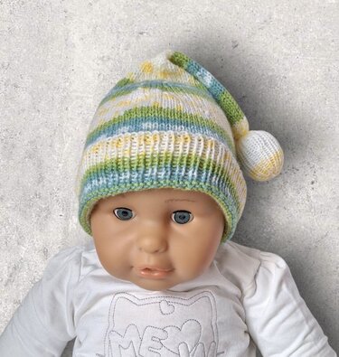 Puppe mit gestrickter Babymütze in Grün, Blau, Gelb und Weiß, mit Rippenbündchen und Zipfel samt Bommel