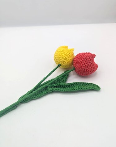 Zwei gehäkelte Tulpen in Rot und Gelb mit grünen Stielen und Blättern auf weißem Hintergrund
