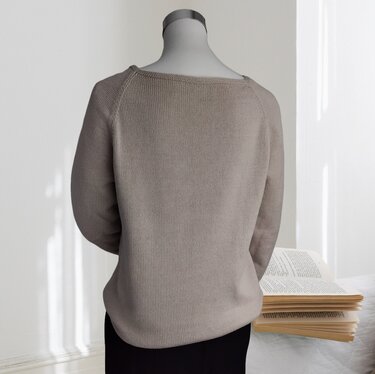 Rückansicht eines beigen, gestrickten Damenpullovers mit Raglanärmeln auf einer Schneiderpuppe; daneben aufgeschlagene Bücher.