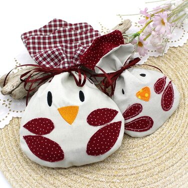 Zwei runde Stoffbeutel in Hühnerform mit roten gepunkteten Applikationen und kariertem Innenfutter auf geflochtener Unterlage