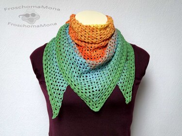 Gehäkeltes Dreieckstuch auf Schaufensterpuppe mit Farbverlauf von Orange über Blau zu Grün und offenem Lochmuster.