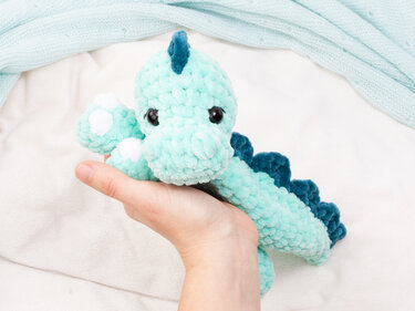 Adult hand holding small mint plush crochet dinosaur showing size