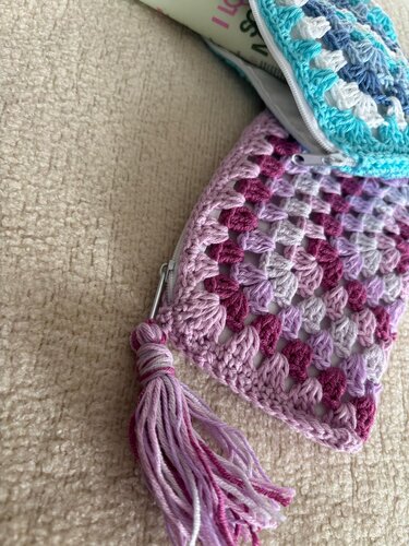 Nahaufnahme eines gehäkelten Granny‑Square‑Etuis in Pastellrosa, Lila und Türkis mit Reißverschluss und Quaste