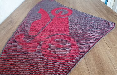 Zweifarbiges Dreieckstuch in Pink und Grau mit stilisiertem Grafikmuster, flach auf hellem Holzboden.