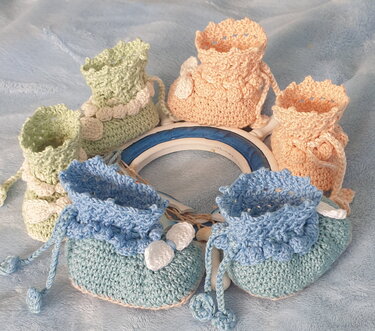 Nahaufnahme gehäkelter Babyschuhe mit Rüschenrand, Zugband und Applikationen in Pastellfarben
