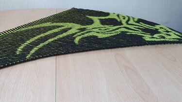 black triangular knitted shawl with neon green motif laid flat on a wooden table
