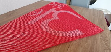 Red triangular knitted shawl with a white deer motif, laid flat on a wooden table.