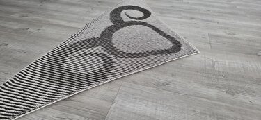 Black and white knitted triangular shawl with striped sections and a large circular motif, laid flat on wooden floor