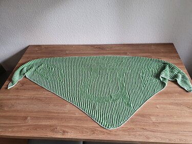 Gestricktes Dreieckstuch mit Ripple-Muster und Streifen in Grün und Weiß, auf einem Holztisch liegend.
