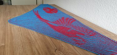 Gestricktes dreieckiges Tuch blau mit roten Monstera- und Palmenmotiven auf Holztisch