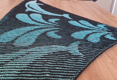 Black and aqua triangular knitted shawl with dolphin and wave motifs.