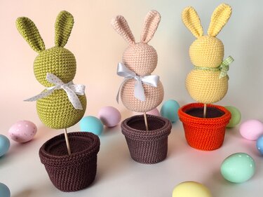 Drei schnell gehäkelte Hasen-Amigurumi in Töpfen, buntes Ostereier-Arrangement