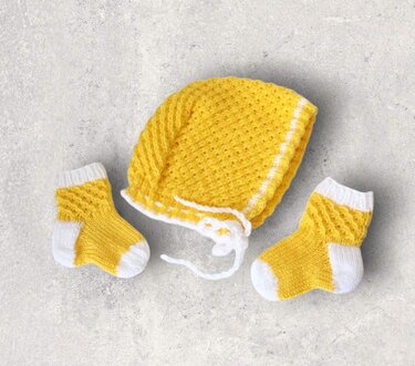 Gestrickte Babymütze mit Bindebändern und zwei gelb-weißen Babysocken auf hellem Untergrund