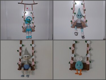 Vier gehäkelte Figuren auf blumengeschmückten Schaukeln zum Aufhängen, darunter Wichtel, eine blaue Figur mit Brille und ein Osterei mit Ohren.